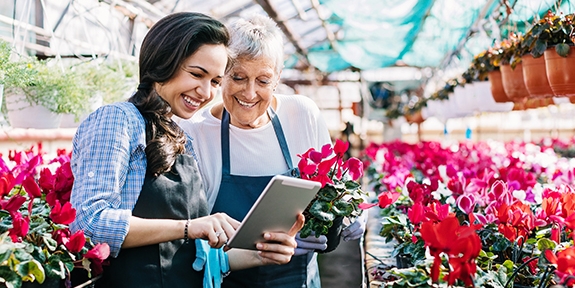 Gardeners with tablet in greenhouse surrounded by flowers