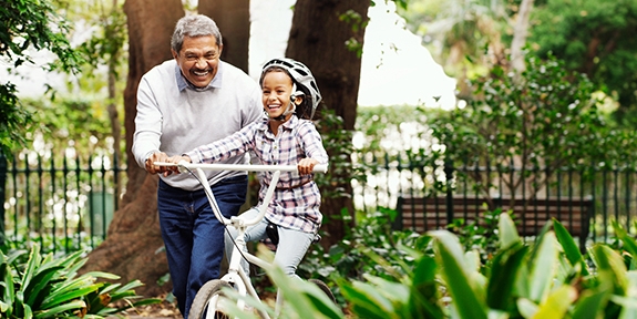 Little girl being taught how to ride a bicycle by her grandfather at the park.