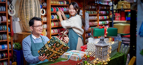 A man and woman working in a festive store that sells bright colorful gift wrapping supplies.