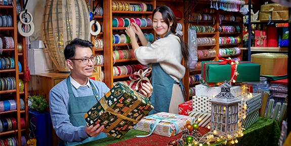 A man and woman working in a festive store that sells bright colorful gift wrapping supplies.