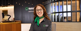 A smiling WaFd Bank representative in a branded shirt and green scarf sits at a desk, providing professional support to business clients.