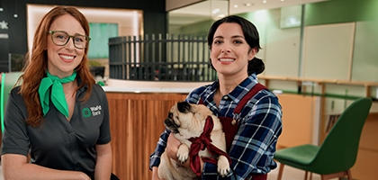 A WaFd Bank employee and a woman holding a pug sit together at a table inside a bank branch.