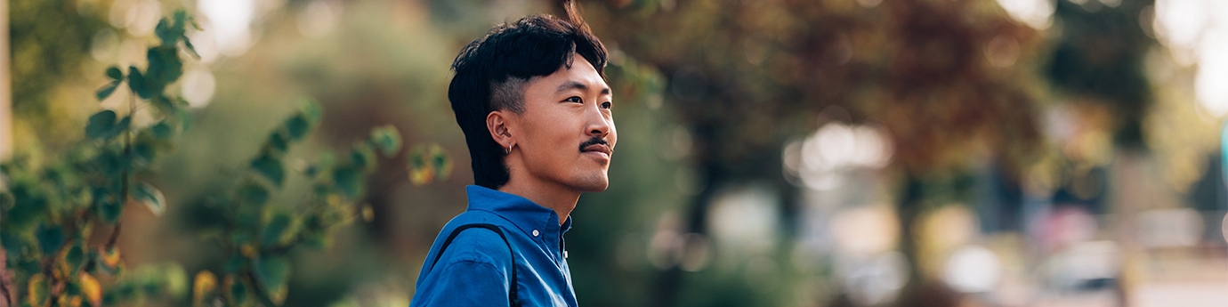 A man in a blue shirt holding a coffee cup while standing outdoors in a park setting.