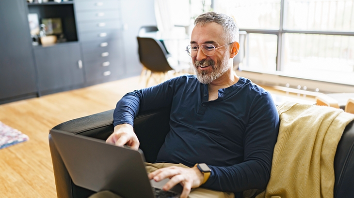 Man sitting on a couch using a laptop.